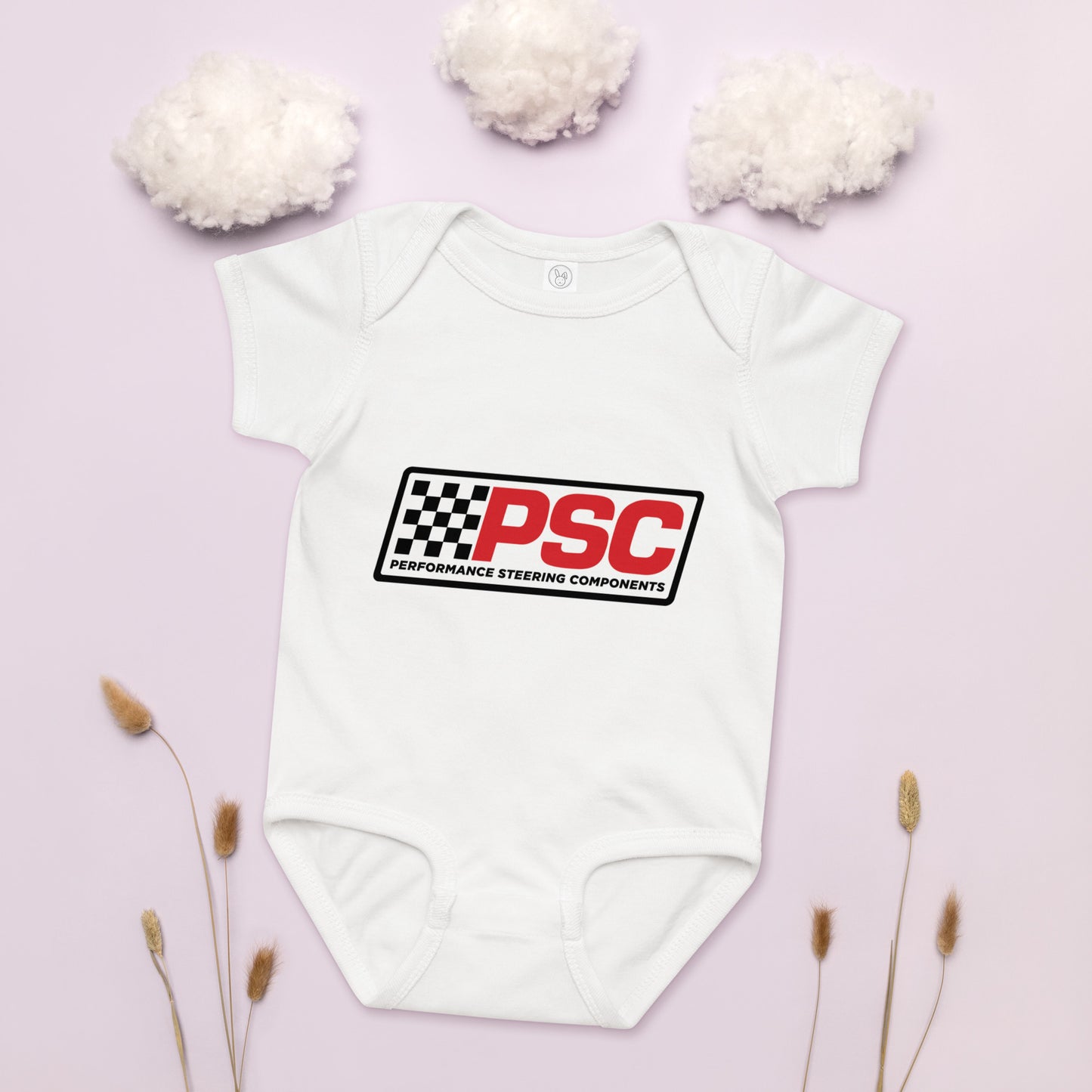 PSC logo white baby bodysuit, jersey material product mockup with a pink background showing cotton as clouds and some plants on the bottom for decoration.