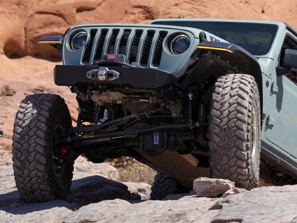 Off-road vehicle navigating rocky terrain with upgraded steering and suspension components for rock crawling applications.
