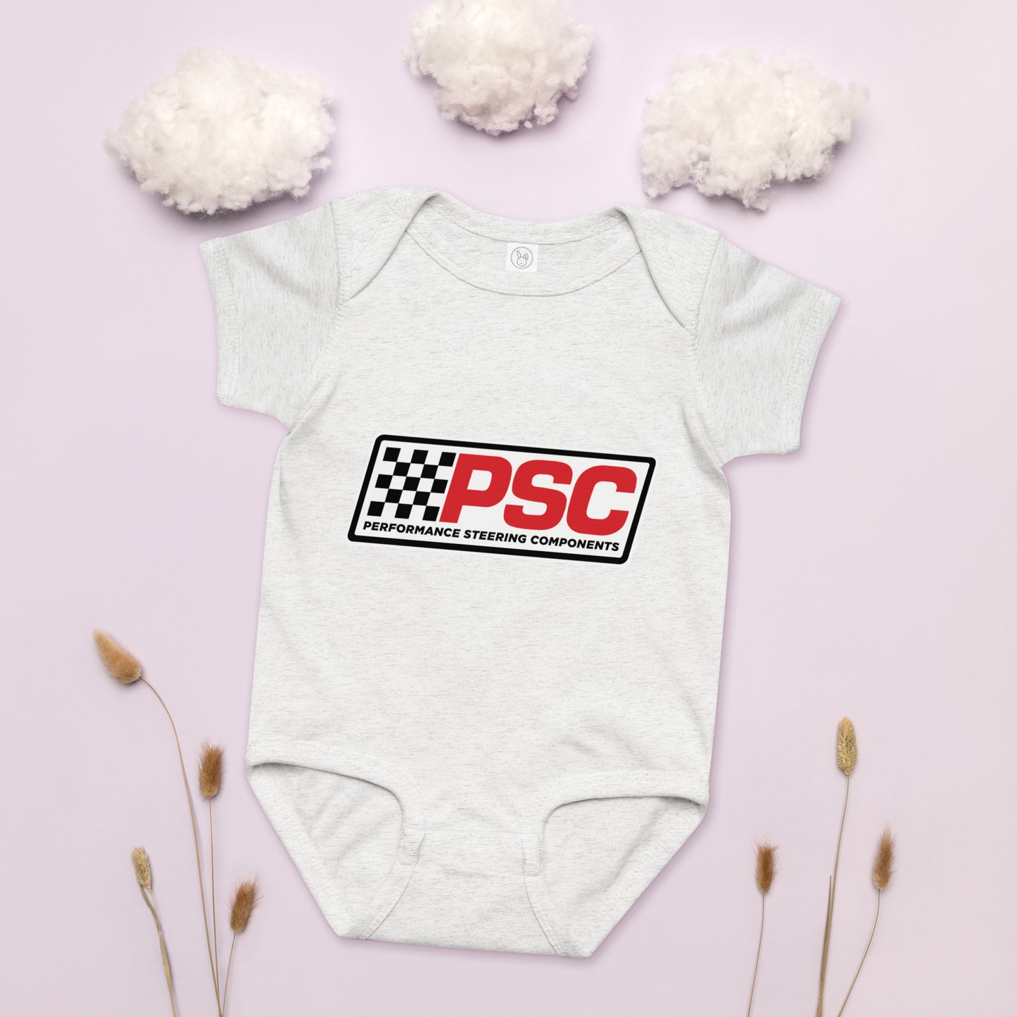 PSC logo ash grey baby bodysuit, jersey material product mockup with a pink background showing cotton as clouds and some plants on the bottom for decoration. 