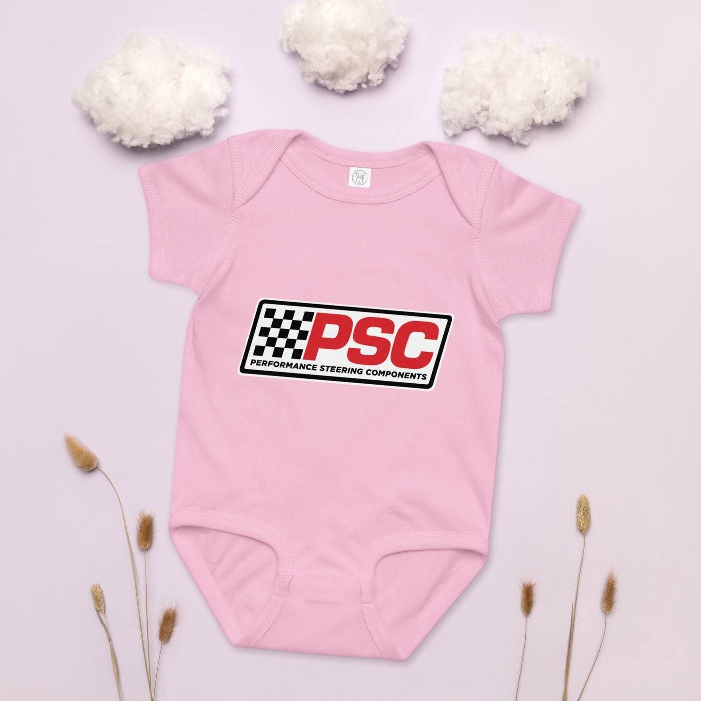 PSC logo pink baby bodysuit, jersey material product mockup with a pink background showing cotton as clouds and some plants on the bottom for decoration. 
