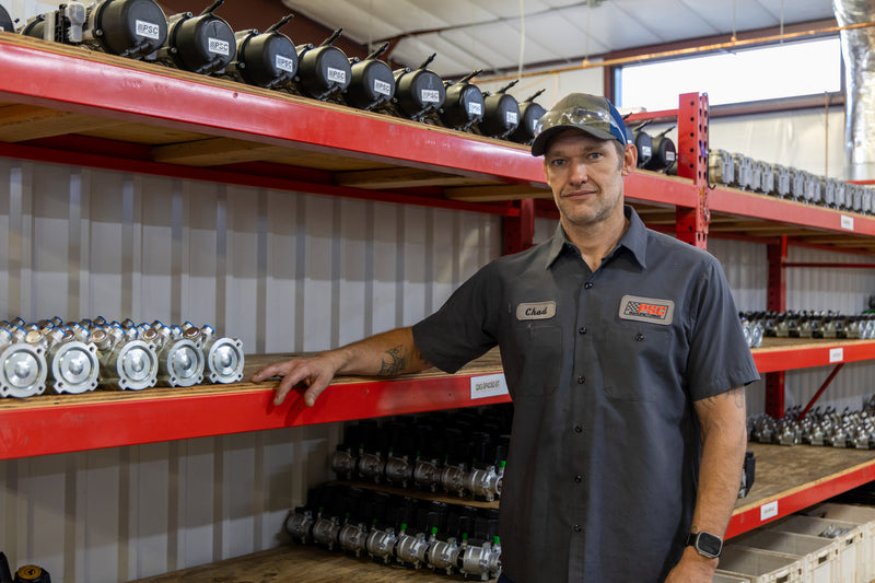 Chad, a PSC technician stands beside shelves stocked with assembled power steering pumps inside the PSC manufacturing facility, highlighting organized inventory, precision-built components and PSC’s commitment to dependable steering solutions for off-road, Jeep and truck applications.