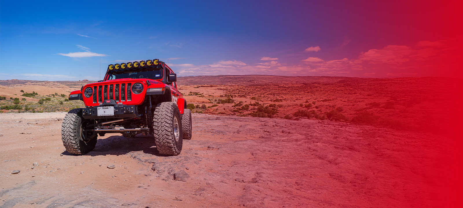 Red PSC Rubicon off-road vehicle on a dirt road with a desert landscape in the background and a red gradient over the right side. 