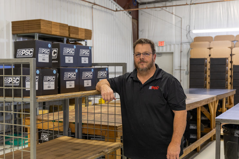 John D, a PSC team member stands beside a rack of boxed PSC steering components in the manufacturing boxing area, showcasing organized packaging, attention to detail and PSC’s commitment to delivering high-quality power steering solutions for off-road, Jeep, truck and performance applications.