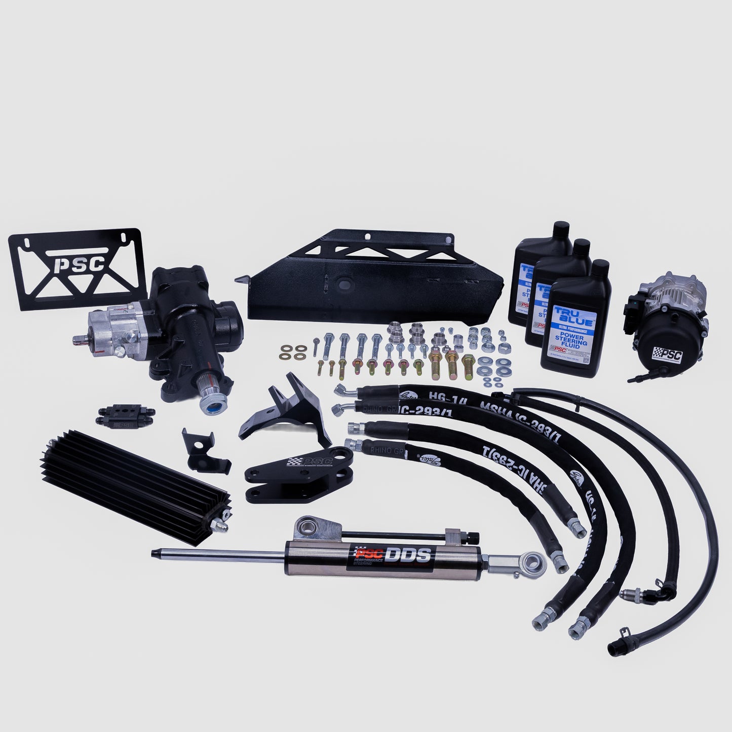 A complete vehicle suspension and steering kit laid out on a light gray background, including a PSC license plate frame, black control arms, a silver and black DDS shock absorber, hydraulic hoses, bushings, mounting hardware, and fluid bottles.