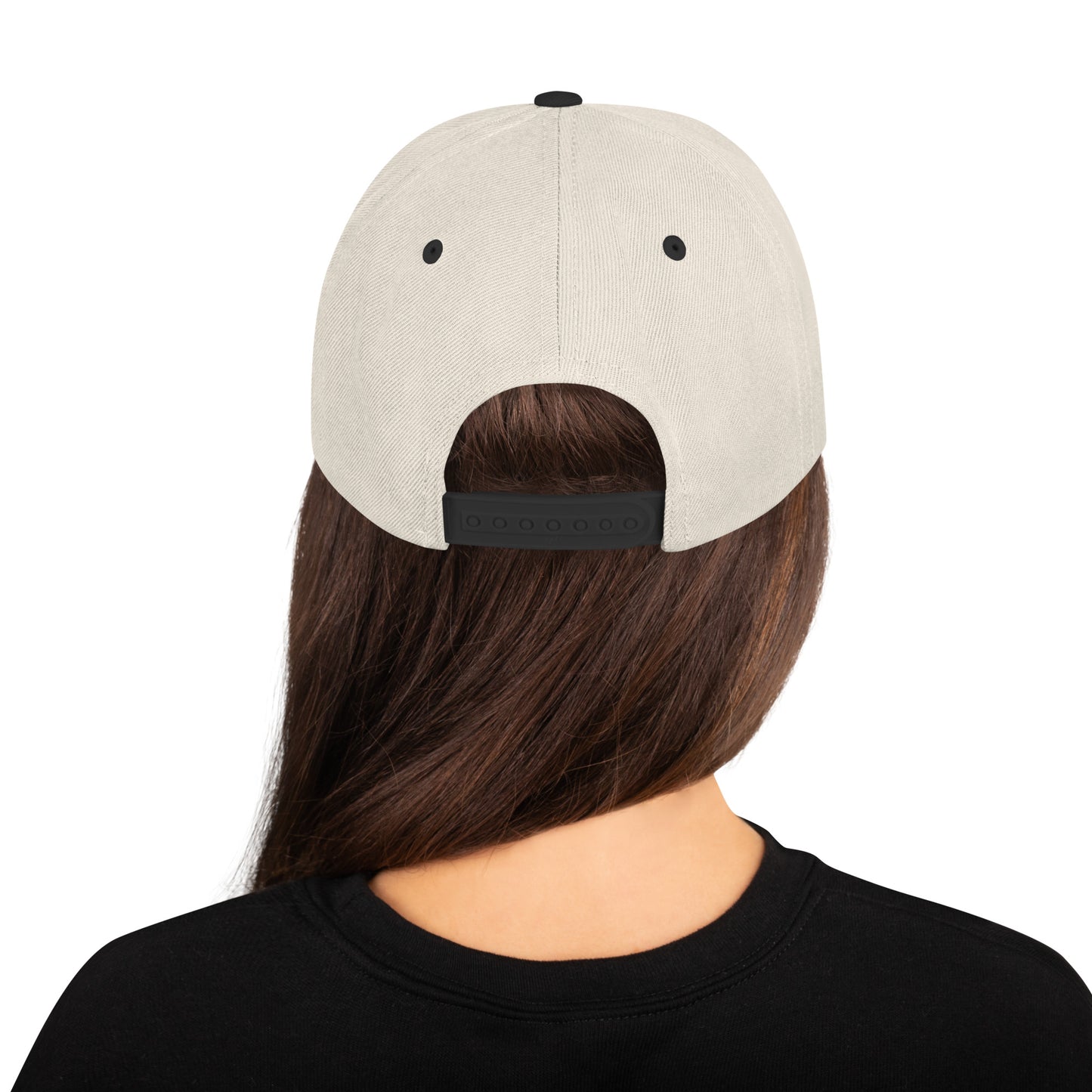 Product mockup image of the back of a classic snapback cap in a neutral tan color with black snap clasps and black bill.  The model is wearing a black t-shirt and background behind her is white. The PSC logo with "PSC" in red, the flag and words "Performance Steering Components" are in back with a white background and black border are embroidered on the center of the cap.