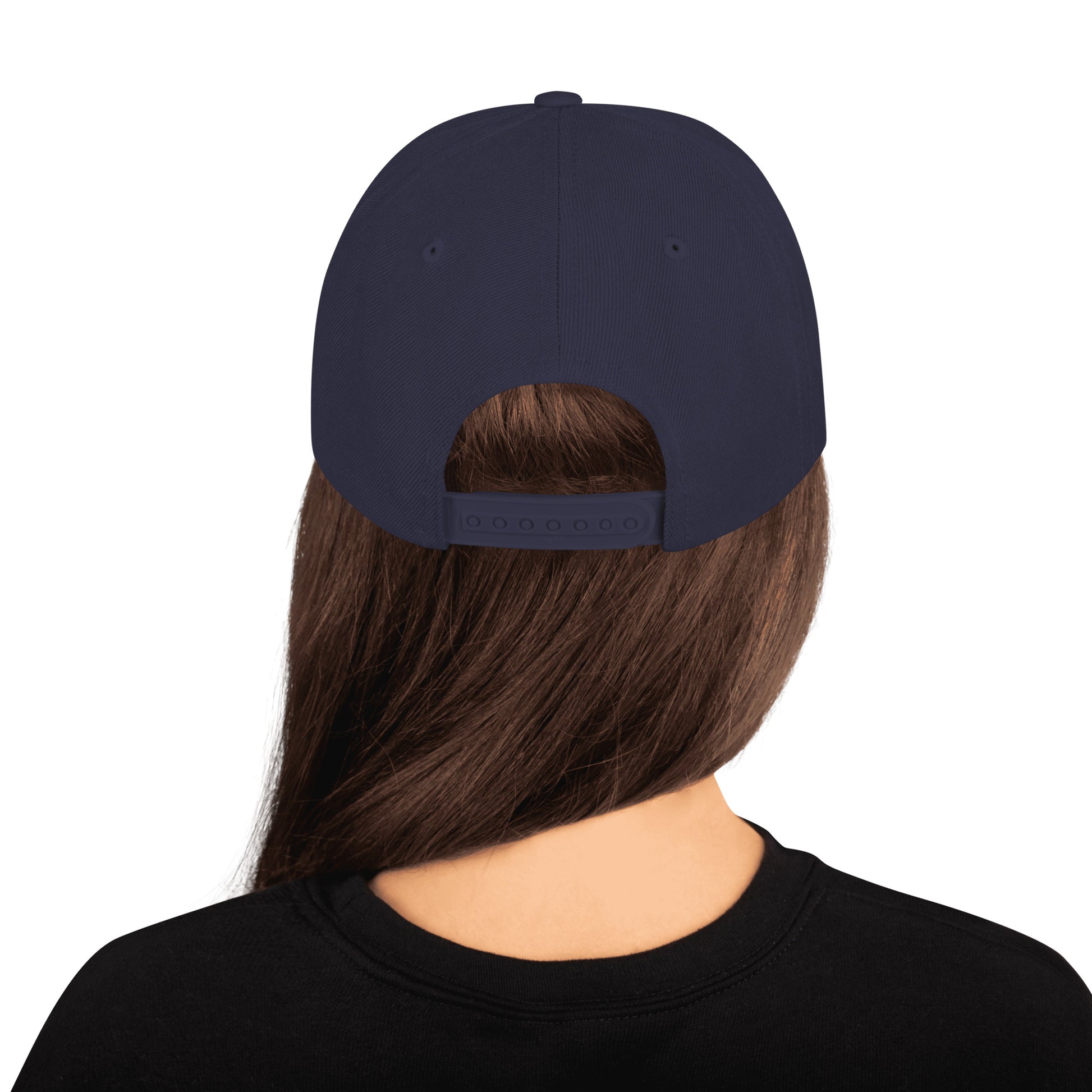 Product mockup image of the back of a classic snapback cap in a navy blue color with navy snap clasps, accents and bill. The PSC logo with "PSC" in red, the flag and words "Performance Steering Components" are in back with a white background and black border are embroidered on the center of the cap. The model is wearing a black t-shirt and background behind her is white.