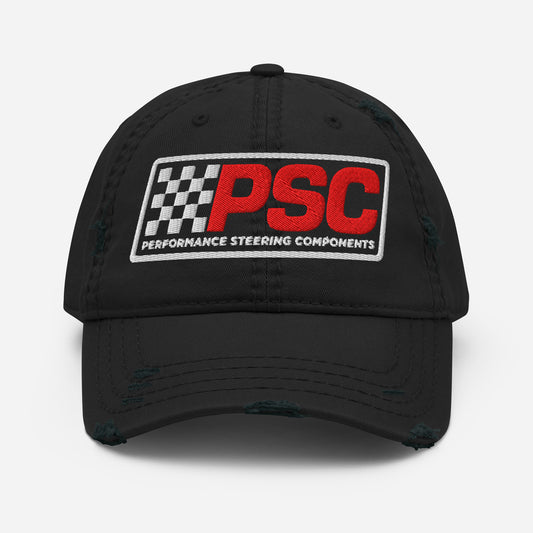 Distressed styled black hat with a PSC logo where the letters are in a bold red and the flag emblem, border and words "Performance Steering Components" are in white. The background of the photo is white. 