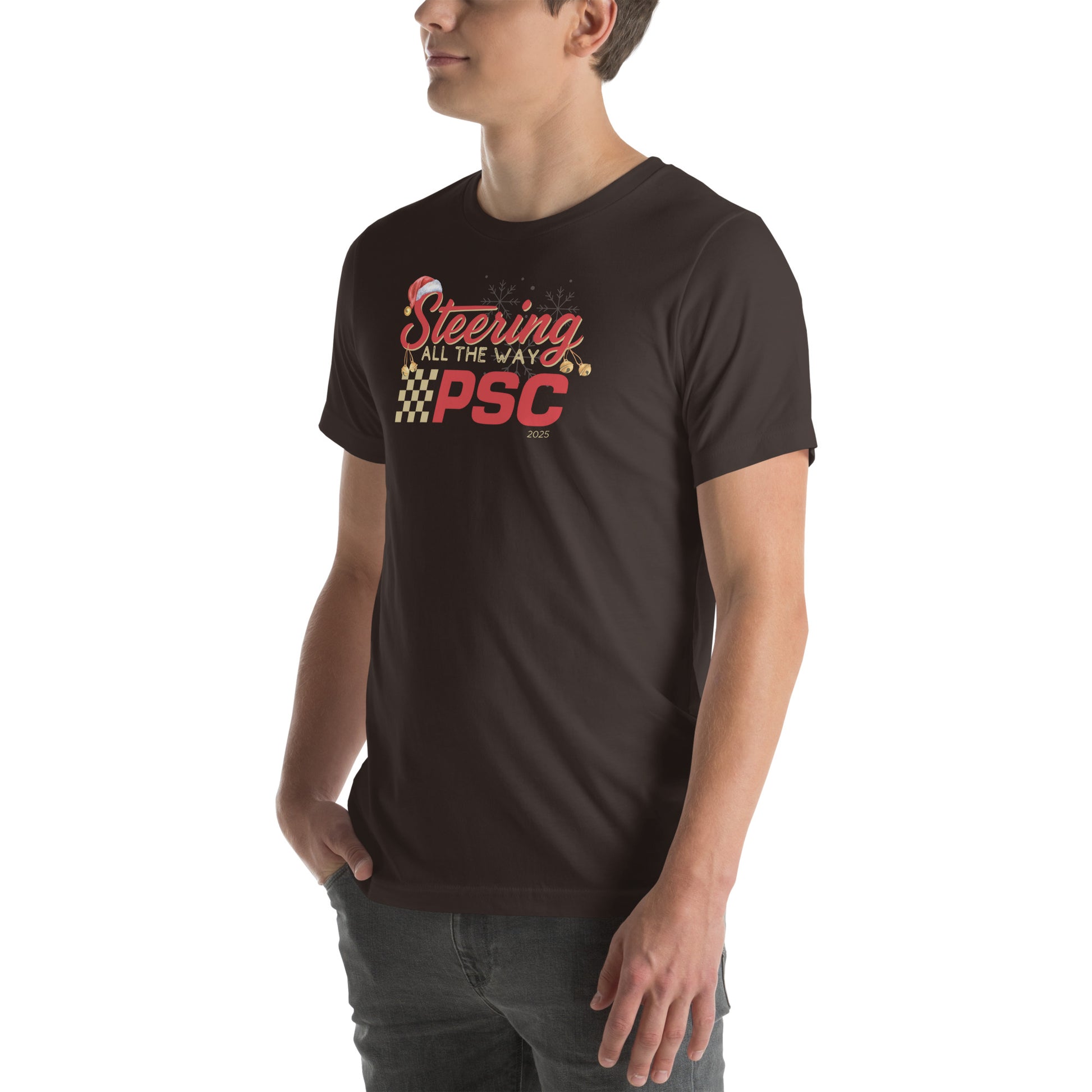 Angled front view of an adult model wearing a brown short-sleeve T-shirt with a PSC logo and the phrase ‘Steering All the Way PSC 2025’ printed across the chest in red and gold lettering. There is a Santa hat on the "S" in steering, bells handing off the bottom of the "S" and "g" in steering and translucent snowflakes in the background as well as "2025" right bottom corner offset. He is facing the left frame of the image.