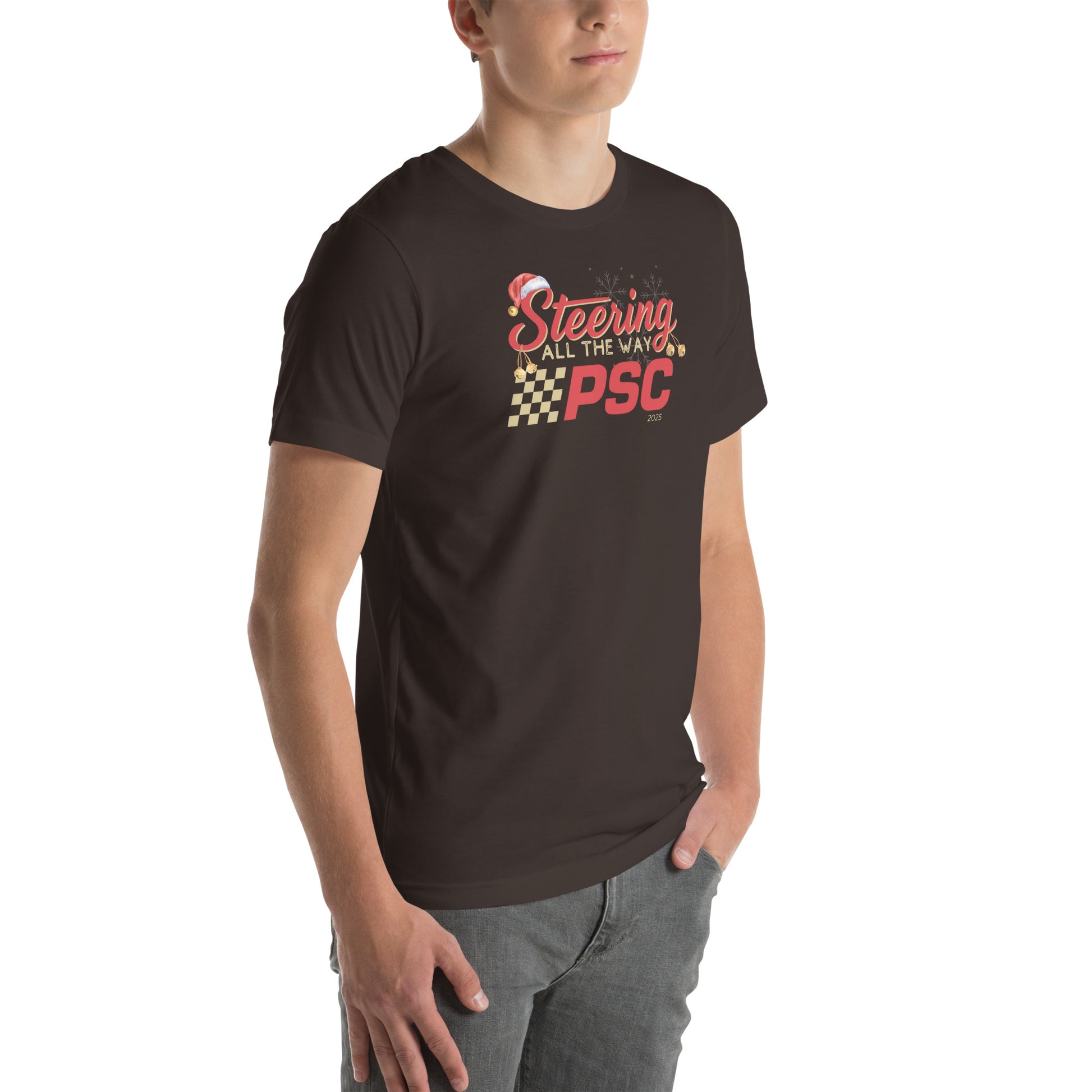 Angled front view of an adult model wearing a brown short-sleeve T-shirt with a PSC logo and the phrase ‘Steering All the Way PSC 2025’ printed across the chest in red and gold lettering. There is a Santa hat on the "S" in steering, bells handing off the bottom of the "S" and "g" in steering and translucent snowflakes in the background as well as "2025" right bottom corner offset. He is facing the right frame of the image.