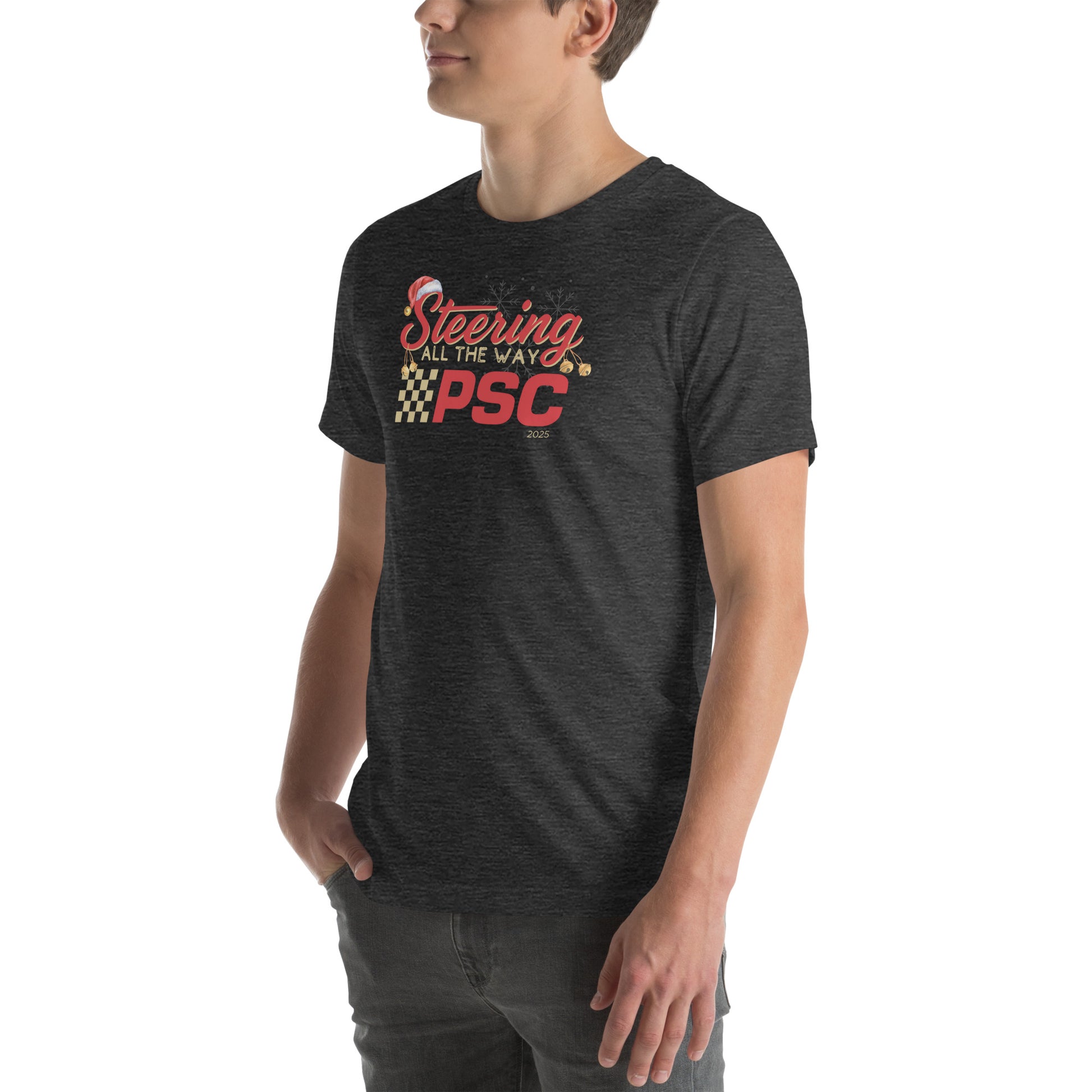 Angled front view of an adult model wearing a heather dark grey short-sleeve T-shirt with a PSC logo and the phrase ‘Steering All the Way PSC 2025’ printed across the chest in red and gold lettering. There is a Santa hat on the "S" in steering, bells handing off the bottom of the "S" and "g" in steering and translucent snowflakes in the background as well as "2025" right bottom corner offset. He is facing the left frame of the image.