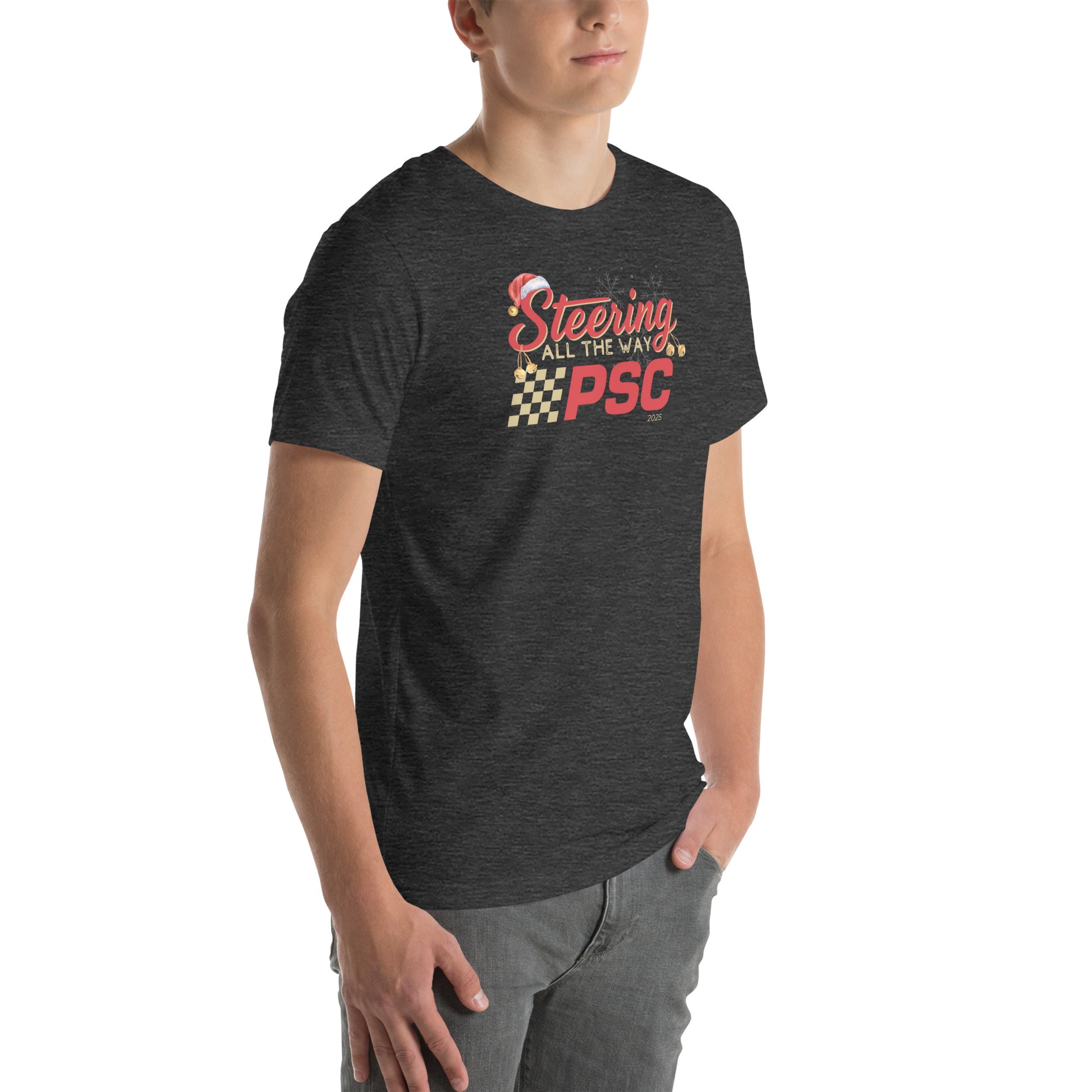Angled front view of an adult model wearing a heather dark grey short-sleeve T-shirt with a PSC logo and the phrase ‘Steering All the Way PSC 2025’ printed across the chest in red and gold lettering. There is a Santa hat on the "S" in steering, bells handing off the bottom of the "S" and "g" in steering and translucent snowflakes in the background as well as "2025" right bottom corner offset. He is facing the right frame of the image.
