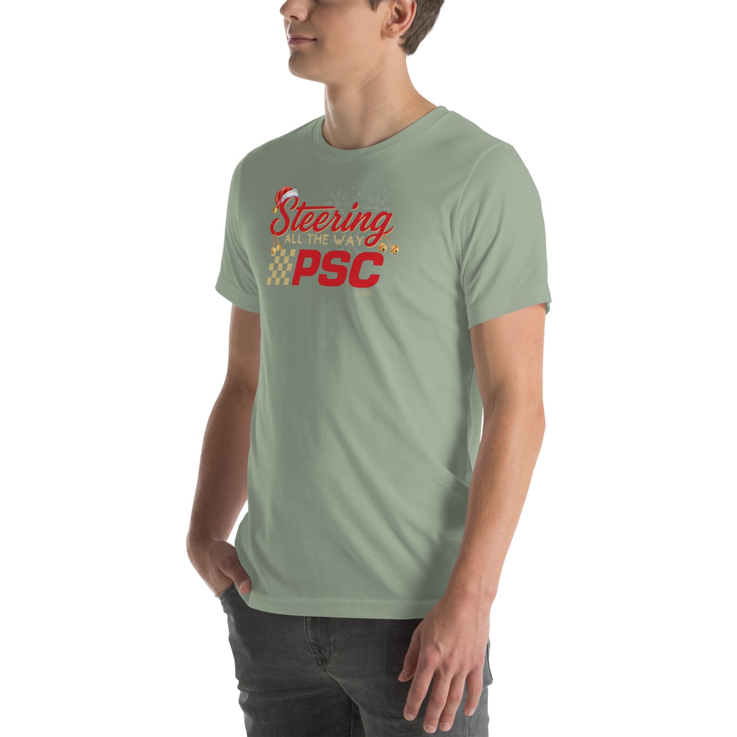 Angled front view of an adult model wearing a sage green short-sleeve T-shirt with a PSC logo and the phrase ‘Steering All the Way PSC 2025’ printed across the chest in red and gold lettering. There is a Santa hat on the "S" in steering, bells handing off the bottom of the "S" and "g" in steering and translucent snowflakes in the background as well as "2025" right bottom corner offset. He is facing the left frame of the image. 