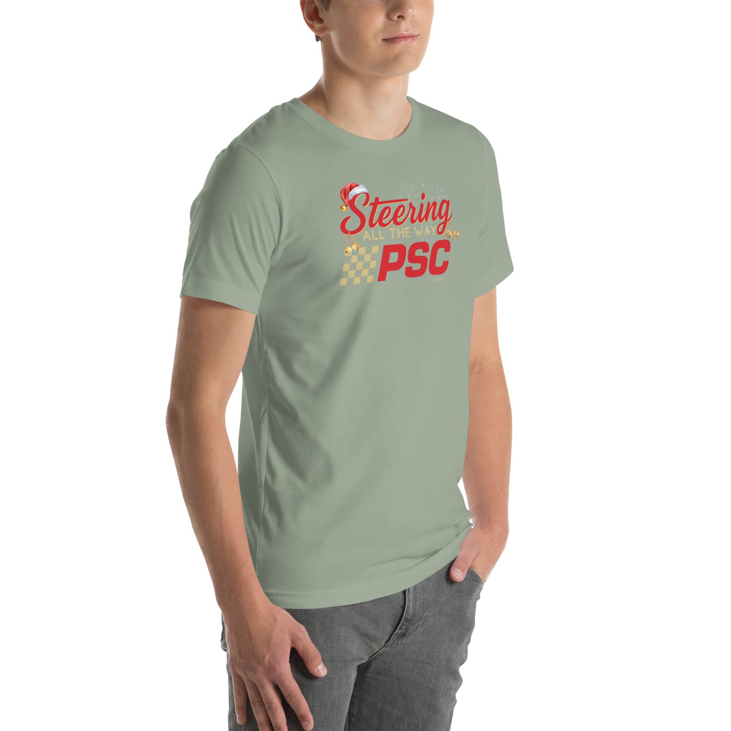 Angled front view of an adult model wearing a sage green short-sleeve T-shirt with a PSC logo and the phrase ‘Steering All the Way PSC 2025’ printed across the chest in red and gold lettering. There is a Santa hat on the "S" in steering, bells handing off the bottom of the "S" and "g" in steering and translucent snowflakes in the background as well as "2025" right bottom corner offset. He is facing the right frame of the image. 